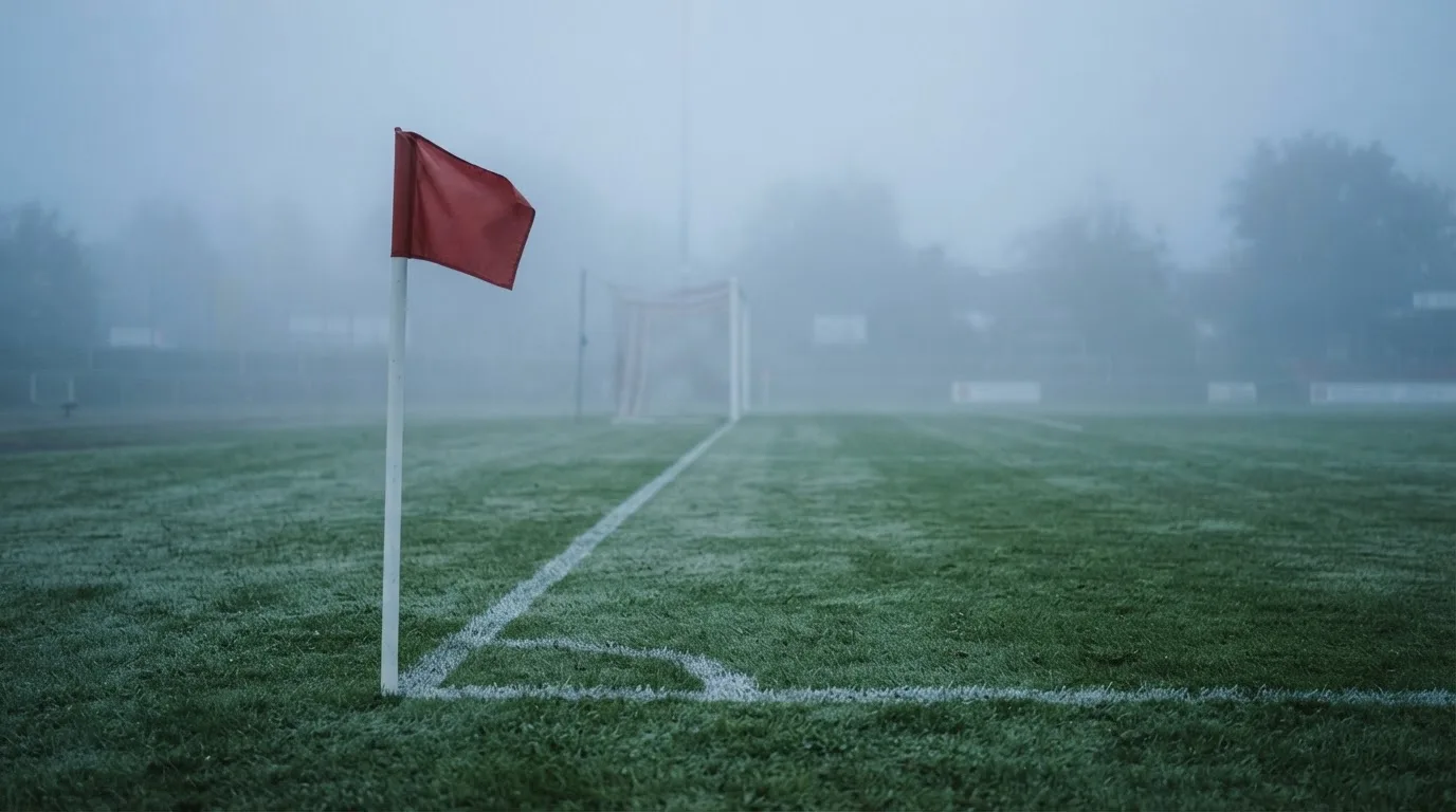 Der Rand eines Spielfelds mit weißer Linie und Eckfahne bei Nebel am frühen Morgen, ohne Menschen.